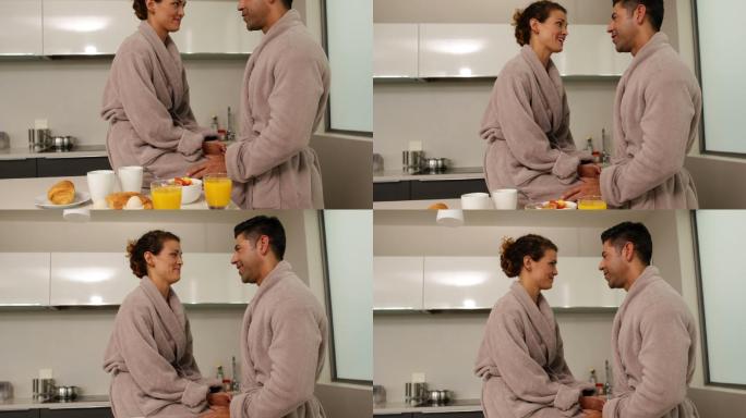 一对幸福的情侣穿着浴袍在家厨房里一起聊天，一起吃早餐