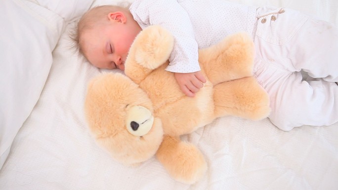 宝宝和泰迪熊在卧室里睡觉