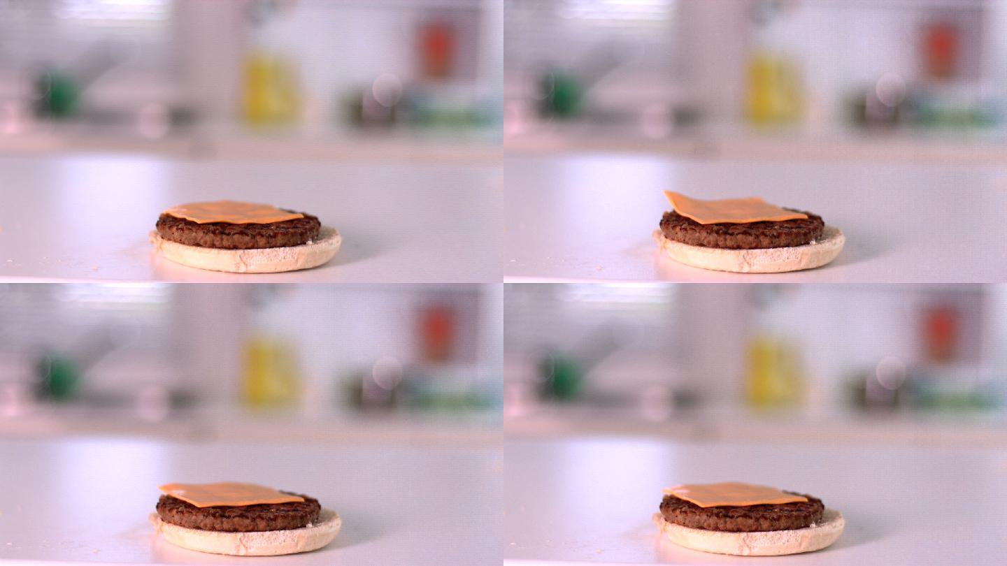 在慢镜头中，一片奶酪落在面包汉堡上