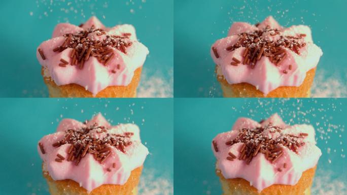 在慢镜头中，粉霜纸杯蛋糕上正在筛糖霜
