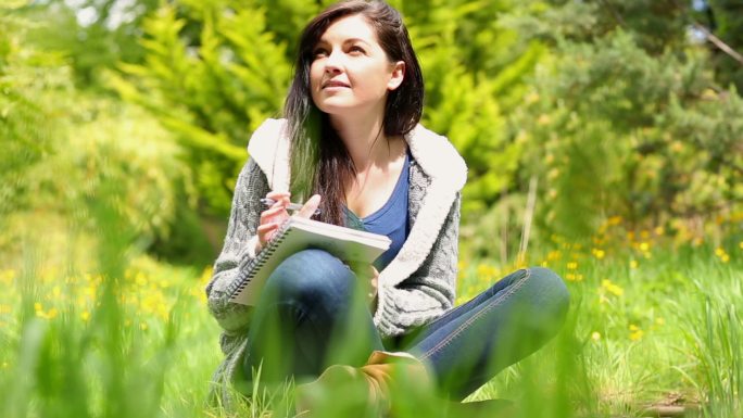 一个阳光明媚的日子，快乐的年轻女子坐在草地上写在记事本上