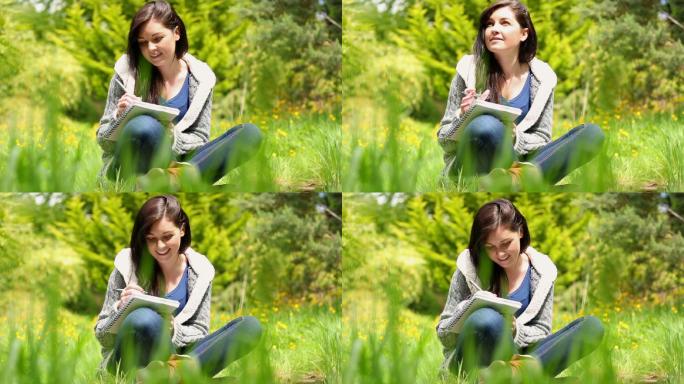 一个阳光明媚的日子，快乐的年轻女子坐在草地上写在记事本上