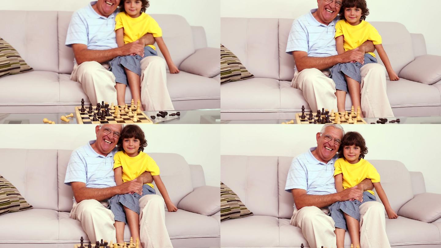 老人坐在沙发上，他的孙子在棋室里下棋