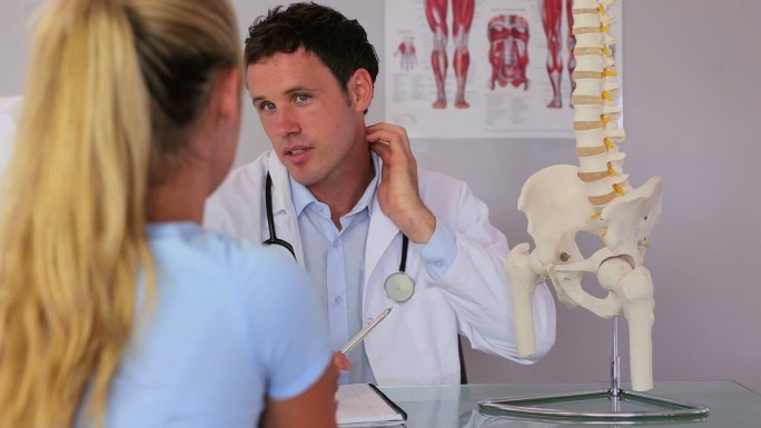 脊椎治疗师与他的病人交谈，并使用脊柱模型解释一些事情