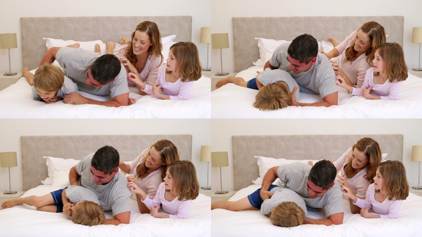 可爱的父母和孩子躺在床上，在卧室里互相开玩笑，逗弄对方