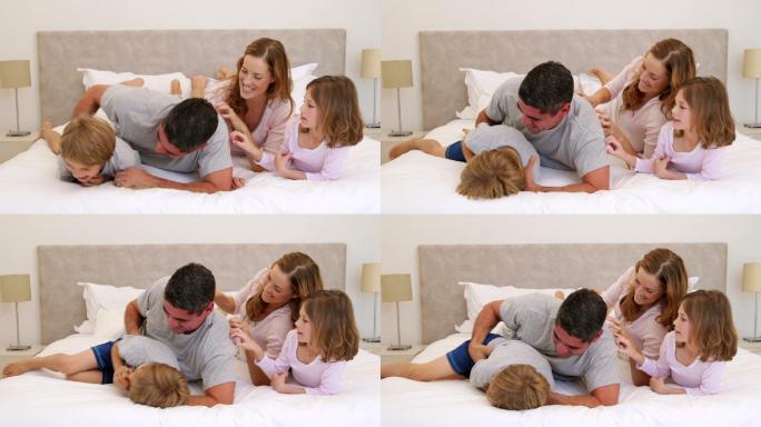 可爱的父母和孩子躺在床上，在卧室里互相开玩笑，逗弄对方