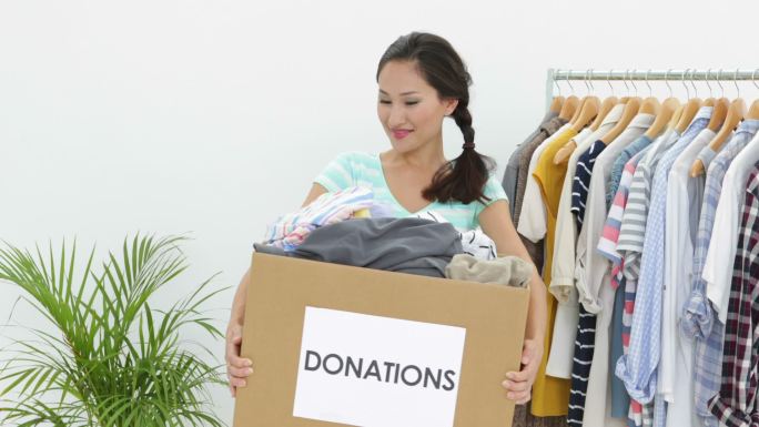 漂亮的亚洲褐发女子拿着捐赠箱装满了衣服对着镜头微笑