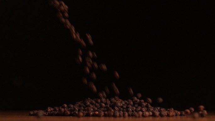 在慢镜头中，胡椒粒倒在黑色背景上