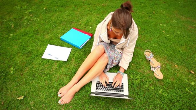 学生坐在校园的草地上用电脑学习特写
