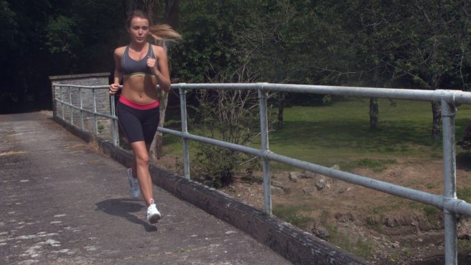 女人穿着运动服在户外桥上跑步特写