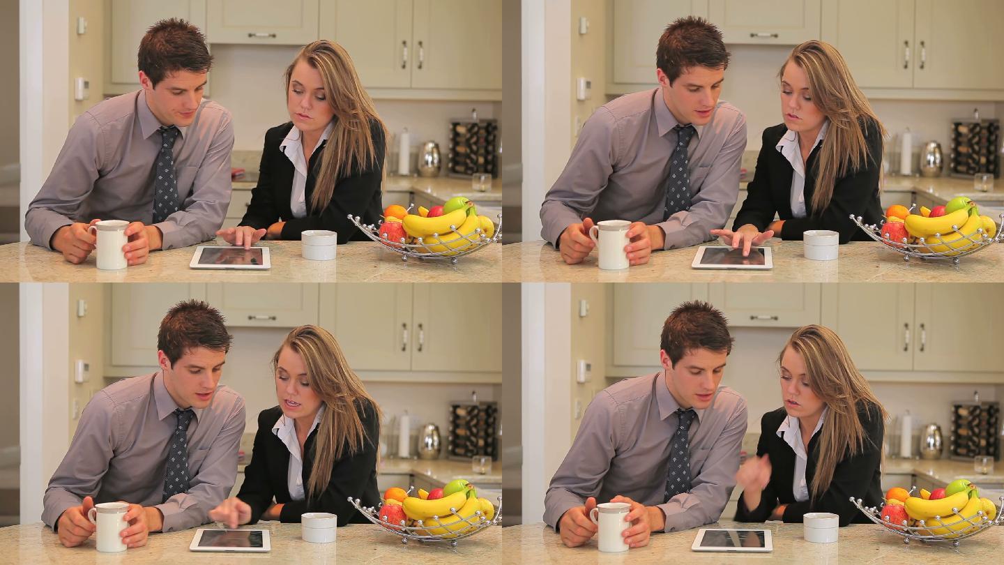 一对夫妇在工作前拿着平板电脑坐在厨房里喝咖啡