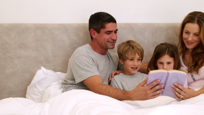 幸福的父母和孩子一起在卧室的床上看书