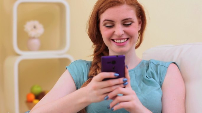 美丽的黑发女人微笑和短信在智能手机在明亮的客厅