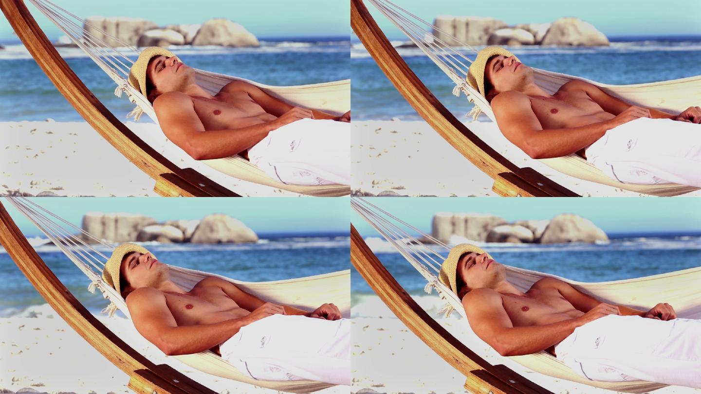英俊的男人躺在沙滩上的吊床上休息