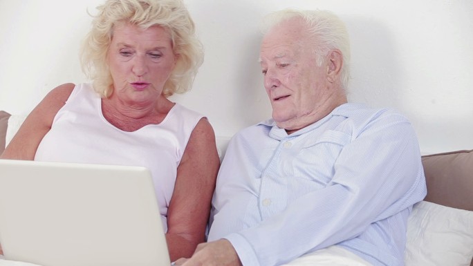 一对老夫妇在卧室里用笔记本电脑聊天