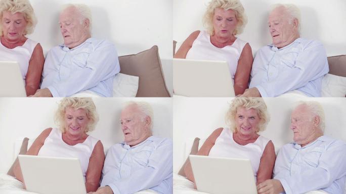 一对老夫妇在卧室里用笔记本电脑聊天