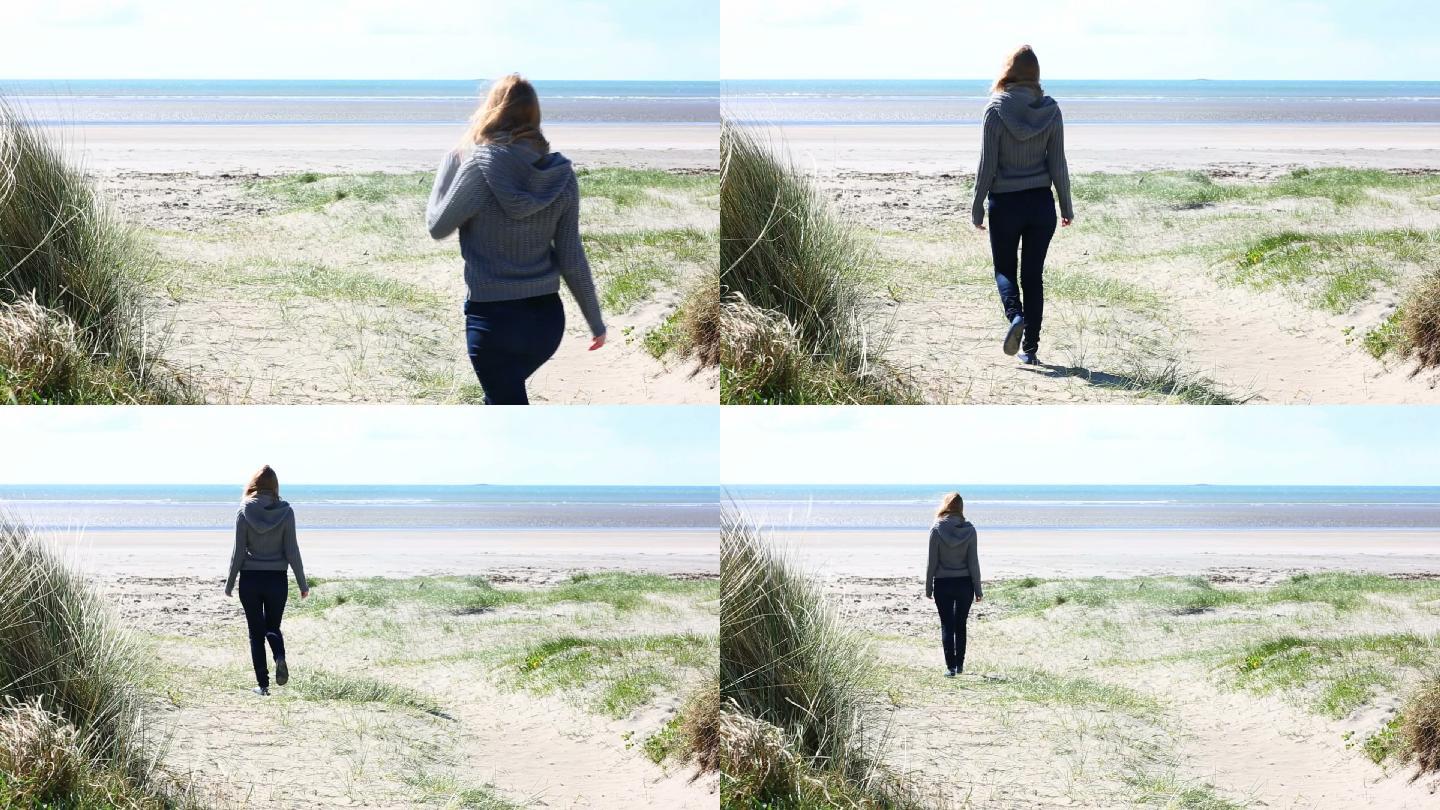 一个女人走在阳光明媚的海滩上