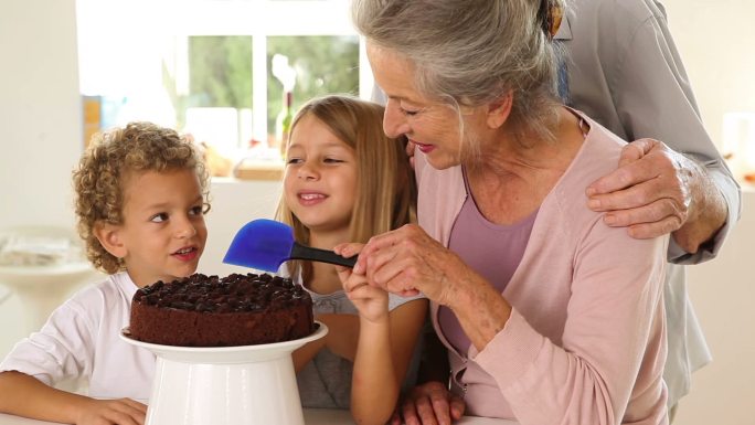 奶奶和孙子们在厨房里给巧克力蛋糕涂糖霜
