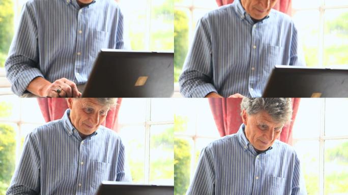 专注的成熟男子坐在窗边使用他的电脑在他的客厅
