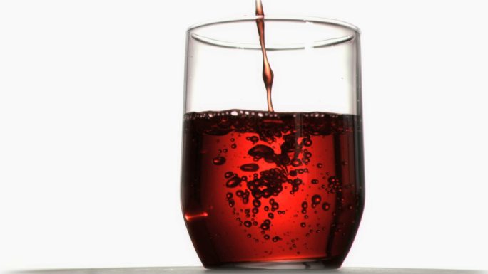 红色液体在白色背景下倒进玻璃杯里特写