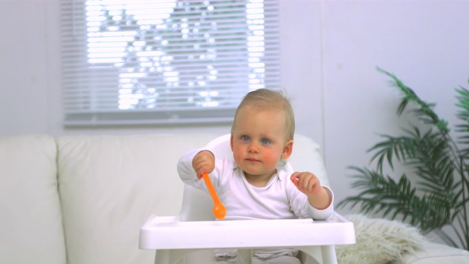 婴儿用勺子轻敲他的高脚椅特写