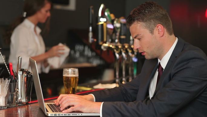 男人一边喝啤酒一边用电脑工作特写