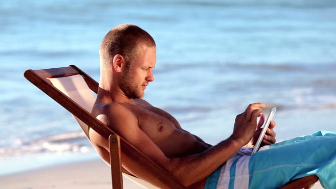 帅哥坐在沙滩上玩平板电脑