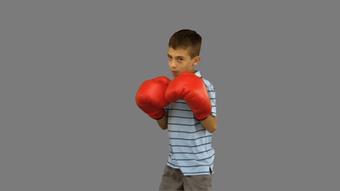 小男孩在灰色背景下戴着手套打拳击特写