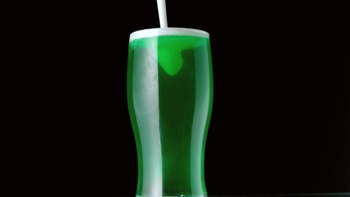 泡沫倒在一杯绿色啤酒上特写