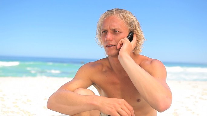男人坐在沙滩上打电话特写