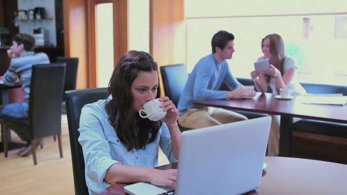 一个女人在大学咖啡馆边喝咖啡边用笔记本电脑打字