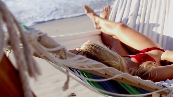 在阳光明媚的海滩上，一个穿着红色比基尼的迷人女子躺在吊床上