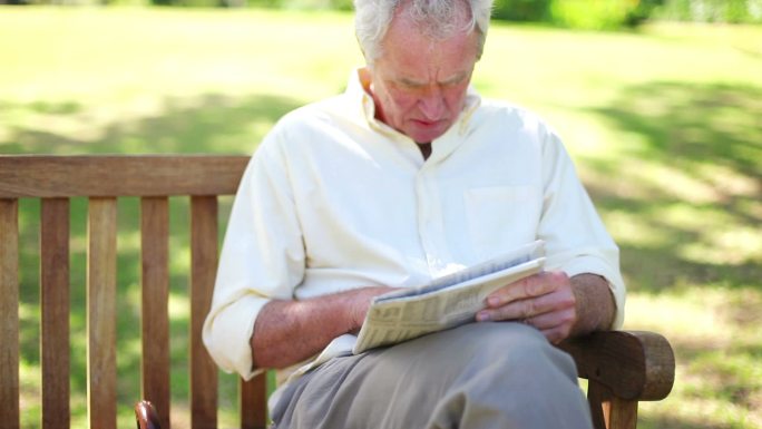 一个退休男子坐在公园的长椅上看报纸特写