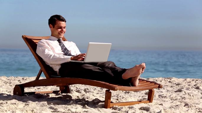 没有压力的商人躺在沙滩上的躺椅上使用笔记本电脑