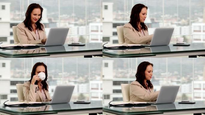 女商人一边喝咖啡一边在笔记本电脑上打字