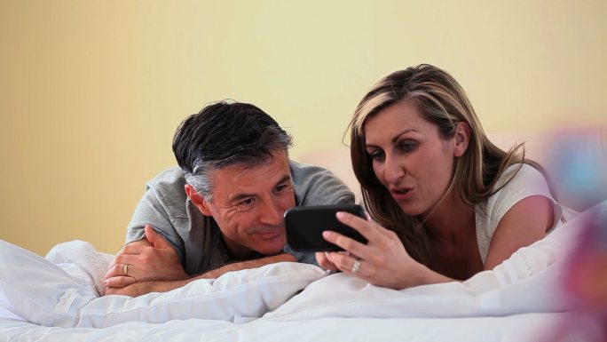 一对夫妇趴在床上看手机特写