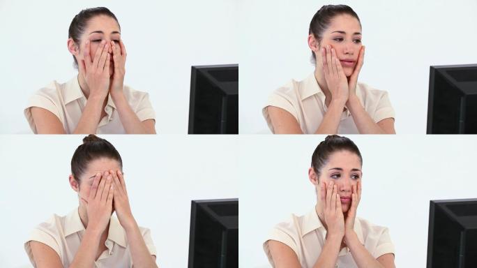 一名年轻女子双手捂着脸，站在电脑前，背景是白色