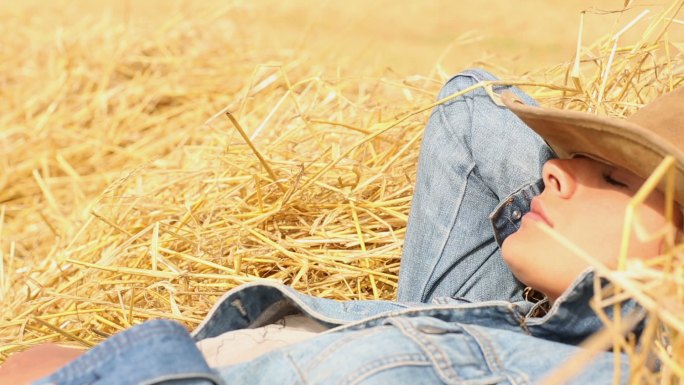 戴着牛仔帽的和平妇女躺在干草中享受阳光
