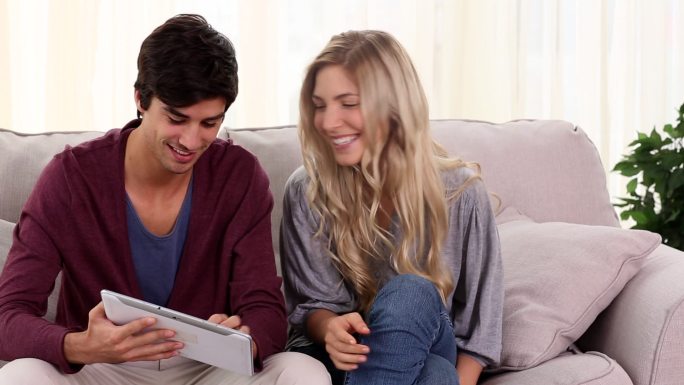 一对夫妇坐在家里的沙发上一起使用平板电脑