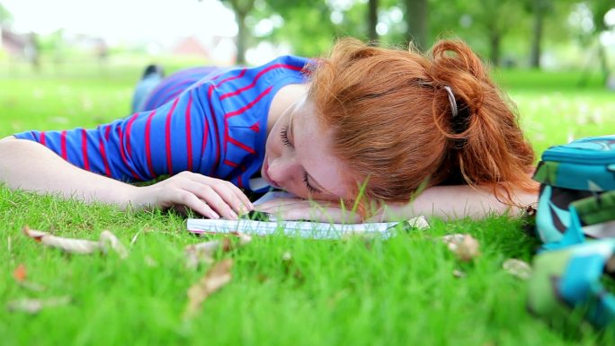一个漂亮的年轻学生躺在大学校园的草地上睡觉