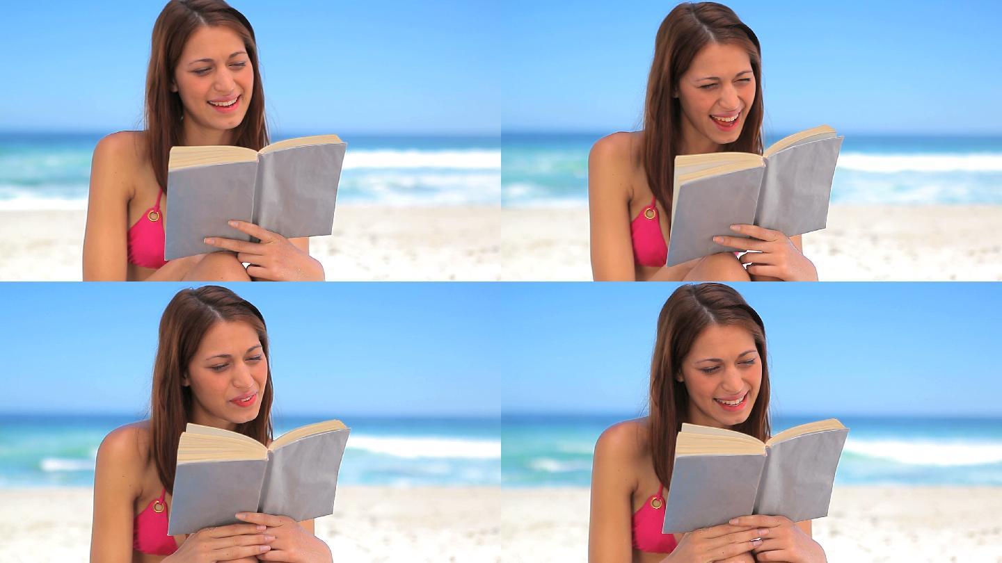 微笑的黑发女子在海滩上读一本有趣的小说