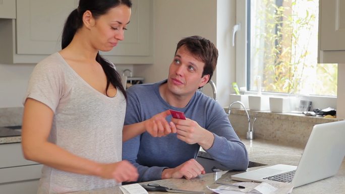 夫妻俩在电脑前讨论财务问题，在厨房里刷信用卡