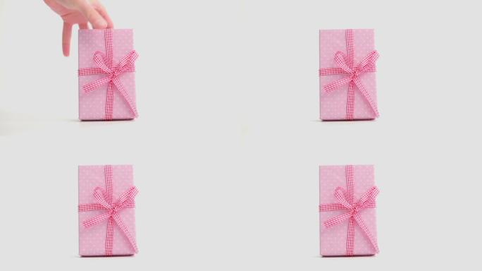 手放下用格子布丝带包裹的粉色礼物，然后在白色背景下拿走