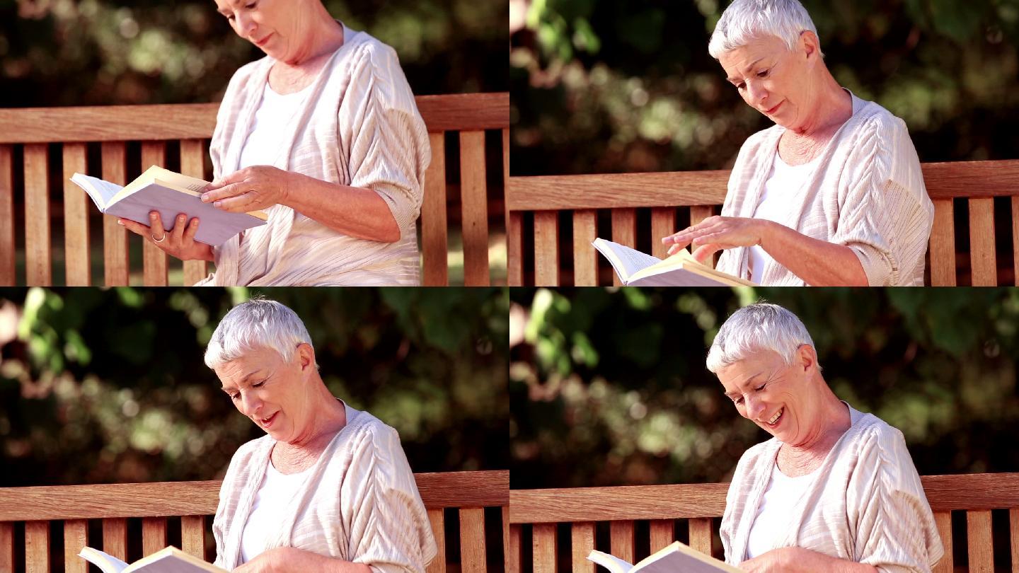 一个老妇人坐在长椅上看书特写