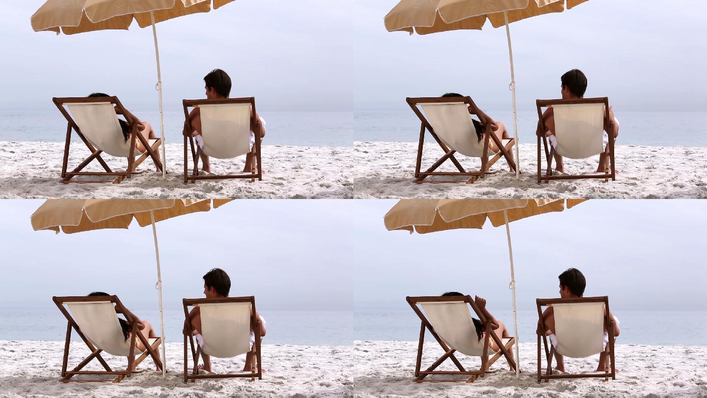 一对情侣躺在沙滩的长椅上特写