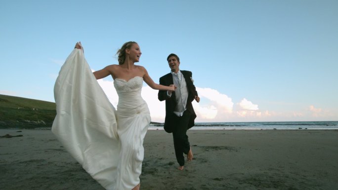 一对快乐的新婚夫妇在沙滩上奔跑的慢镜头