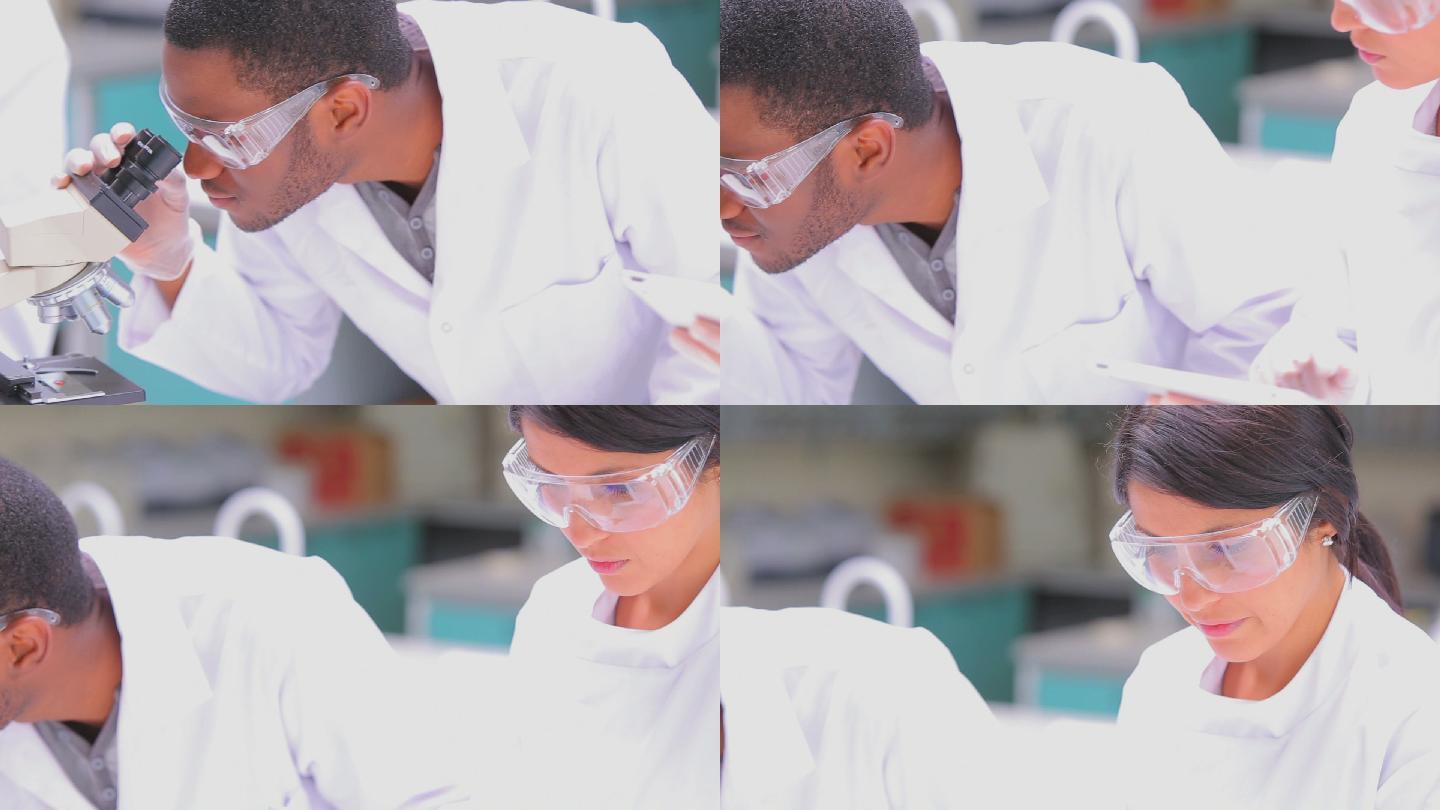 一个学生在实验室里透过显微镜看东西，而他的老师在跟他说话
