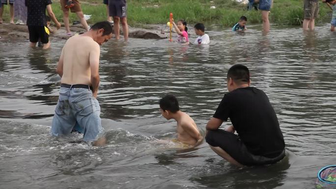 炎热的夏天大人领着小孩子在河中泡澡玩耍
