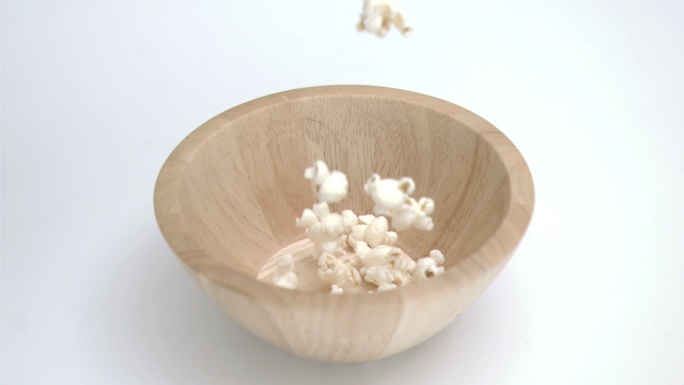 爆米花在白色背景下以超慢镜头落在碗里