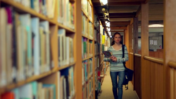 女生抱着书走在图书馆里特写